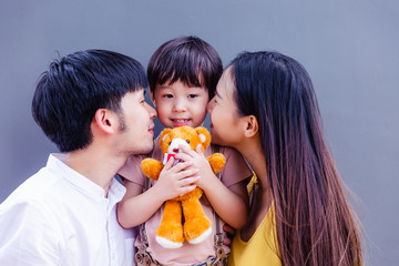 Father and mother kissing kid, child or son with love. Cute little boy is first child of family. Adorable kid hold teddy bear. It happy family time, good memory for children and parents. Happy family