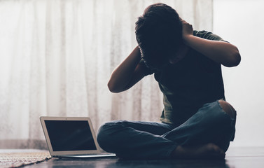Cyberbullying concept. Young Asian preteen/teenage boy sit cross legged alone next to computer...