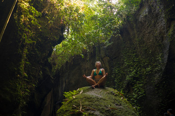 attractive and happy mid adult woman with grey hair 40s or 50s enjoying blissful and free sitting in lotus yoga pose at beautiful green forest feeling the purity of nature