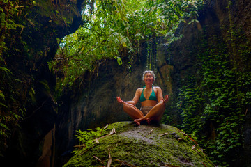 attractive and happy mid adult woman with grey hair 40s or 50s enjoying blissful and free sitting in lotus yoga pose at beautiful green forest feeling the purity of nature