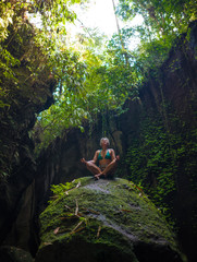 attractive and happy mid adult woman with grey hair 40s or 50s enjoying blissful and free sitting in lotus yoga pose at beautiful green forest feeling the purity of nature