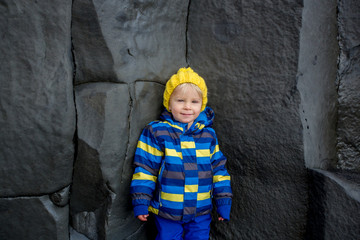 Obraz na płótnie Canvas Toddler posing on the rock of black sand beach of Reynisfjara and the mount Reynisfjall in Iceland on a cold winter day