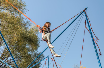 Little charming girl child on elastic ropes jumps on a trampoline in an amusement park