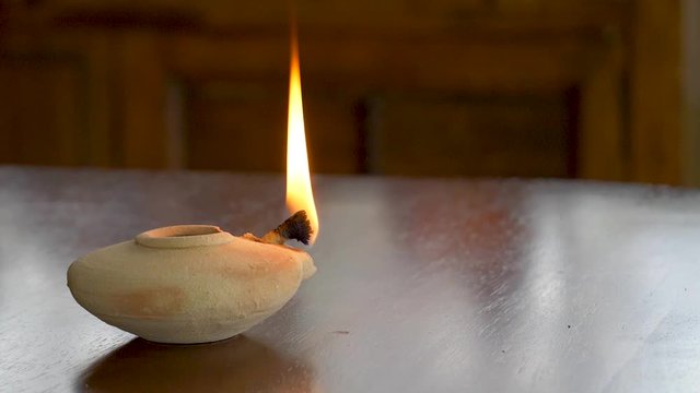 A clay oil lamp of biblical times remains lit in spite of strong wind or an attempt to blow it out - concept faith, hope, belief