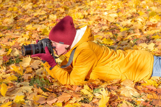 Photographer woman lies on autumn grass with a camera in her hands for taking pictures