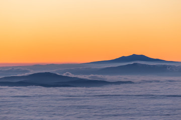 Distant mountains above a sea of fog like islands at sunset