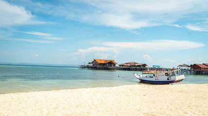 Obraz premium Beautiful view of crystal clear water, white sand, blue sky, traditional cottage, and wooden boat at Derawan Island, Indonesia