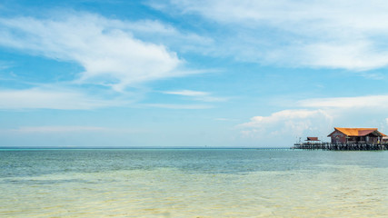 Fototapeta premium Beautiful view of crystal clear water, white sand, blue sky, traditional cottage, and wooden boat at Derawan Island, Indonesia