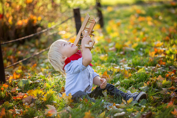 Beautiful blonde two years old toddler boy, playing with wooden plane and teddy bear in the park on sunset