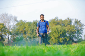 Indian farmer spraying pesticides in green wheat field 