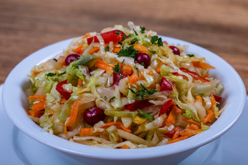 Homemade sauerkraut with carrots, peppers and cranberries in plate. Fresh cabbage salad with carrots and cranberries in a white bowl, closeup