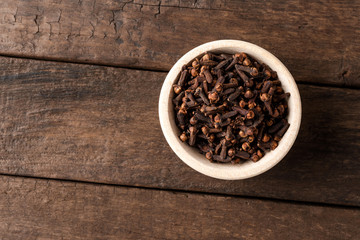 Dried cloves in bowl on wooden table. Close up. Top view