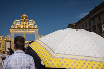 des touristes avec une ombrelle font la queue devant un portail doré pour visiter le château de...