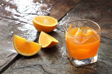 Orange Juice glass on a stone background along with the fresh fruit pieces.