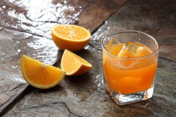 Orange Juice glass on a stone background along with the fresh fruit pieces.