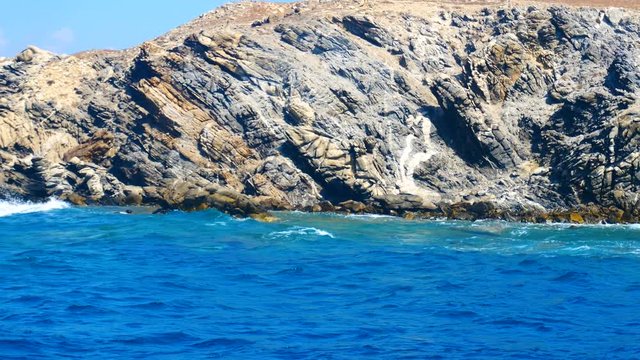 Eroded cliffs and rocks at steep coastline with blue sea, view from a boat.