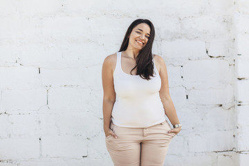 Plus size model dressed in white shirt posing over brick wall