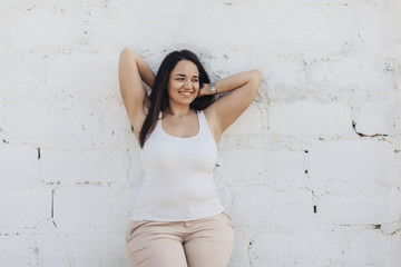 Plus size model dressed in white shirt posing over brick wall