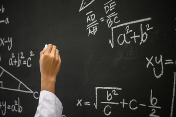 The hand that writes the formula with white chalk on the blackboard