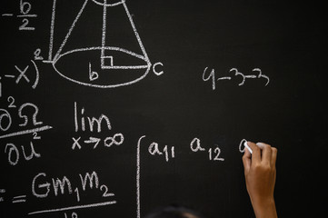 The hand that writes the formula with white chalk on the blackboard