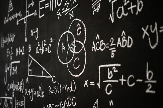 Blackboard inscribed with scientific formulas and calculations in physics, mathematics and electrical circuits. Science and education background.