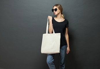 Young woman holding white textile eco bag against gray background. Ecology or environment...