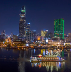 Fototapeta na wymiar Classic night skyline under full lights of Ho Chi Minh City with Saigon river and large tourist boat