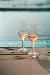 Two glasses of wine  on the edge of infinity swimming pool with panoramic views of the sea at sunset. Drink, celebrate, vacation and summer concept.