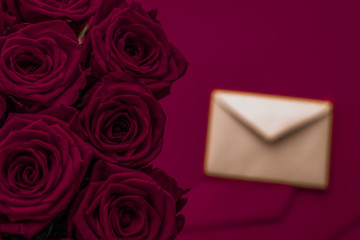Love letter and flowers delivery on Valentines Day, luxury bouquet of roses and card on maroon...