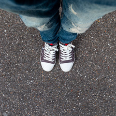 A young man's legs dressed in jeans and tennis on a background of asphalt.