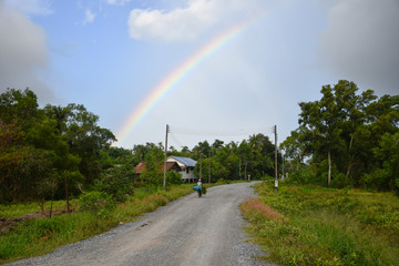 farmer ride bicycle with a grass for animal on rural road and the rainbow on the sky