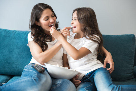 mother and daughter share each other popcorn while watching cartoon on the sofa