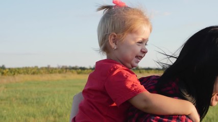 Happy family, mother and child have fun outdoors in the Park. The little lovely blonde girl is having fun and hugs and kisses her mother.