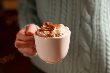 Woman holding mug of cocoa drink with whipped cream in hands