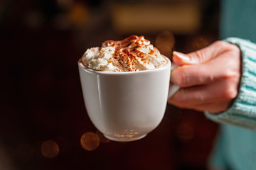 Woman holding mug of cocoa drink with whipped cream in hands
