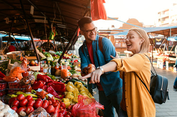 Beautiful young couple buying fresh vegetables on outdoor market.