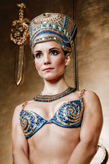 Beautiful thin Egyptian woman with pronounced cheekbones in a huge gold headdress without hair in a blue swimsuit on the background in the Studio