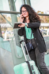 Black-haired girl traveling with luggage. Business woman goes on business trip. Black jacket and blue suitcase.