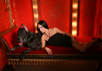 Beautiful young woman posing with her Great Dane dog in the studio in the red room on the couch