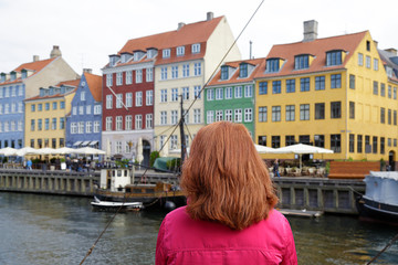 Fototapeta na wymiar Woman enjoying the scenic view of Nyhavn pier. Colorful building facades with boats and yachts in the Old Town of Copenhagen, Denmark