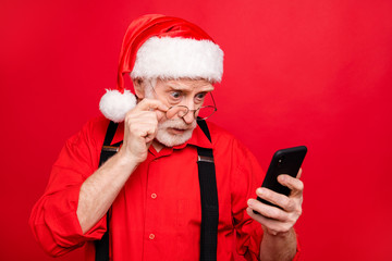 Close-up portrait of his he nice wondered stunned bearded Santa Claus using digital device reading feednews internet online isolated over bright vivid shine vibrant red background