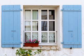 Fototapeta na wymiar Old window with wooden blue painted open shutters decated with flowers in the Island of Re