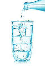 Pouring water from a glass bottle into glass with ice cubes isolated on white