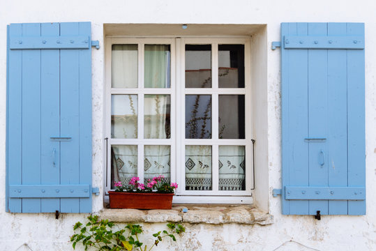 Old window with wooden blue painted open shutters decated with flowers in the Island of Re