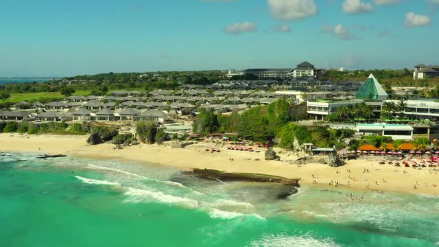 Dreamland beach one of the most beautiful sand beach Bali with happy travel tourist resting under umbrella and surfers in crystal clear sea water. Aerial view. Shot in 4K on Hasselblad, H.265