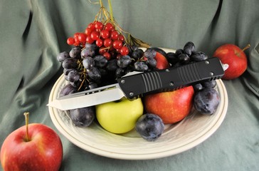 Folding knife stainless steel blade and fresh organic ripe fruits apples grape plums berries natural gourmet product dessert background