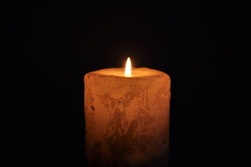 A large candle burns in the dark. On a black background