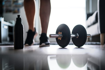 Fototapeta na wymiar Fitness, home workout and weight training concept. Man starting to exercise with dumbbell. Water or protein shake bottle on floor.