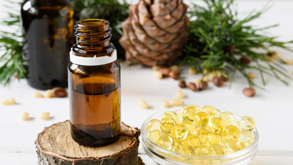 composition of cedar oil with pine nuts on a background of a branch with a pine cone, on a light wooden background