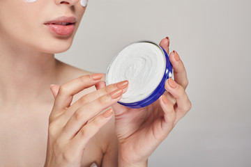 Close-up of a young girl with clean skin holds a cream in both hands in a blue jar. Spa and skin care.